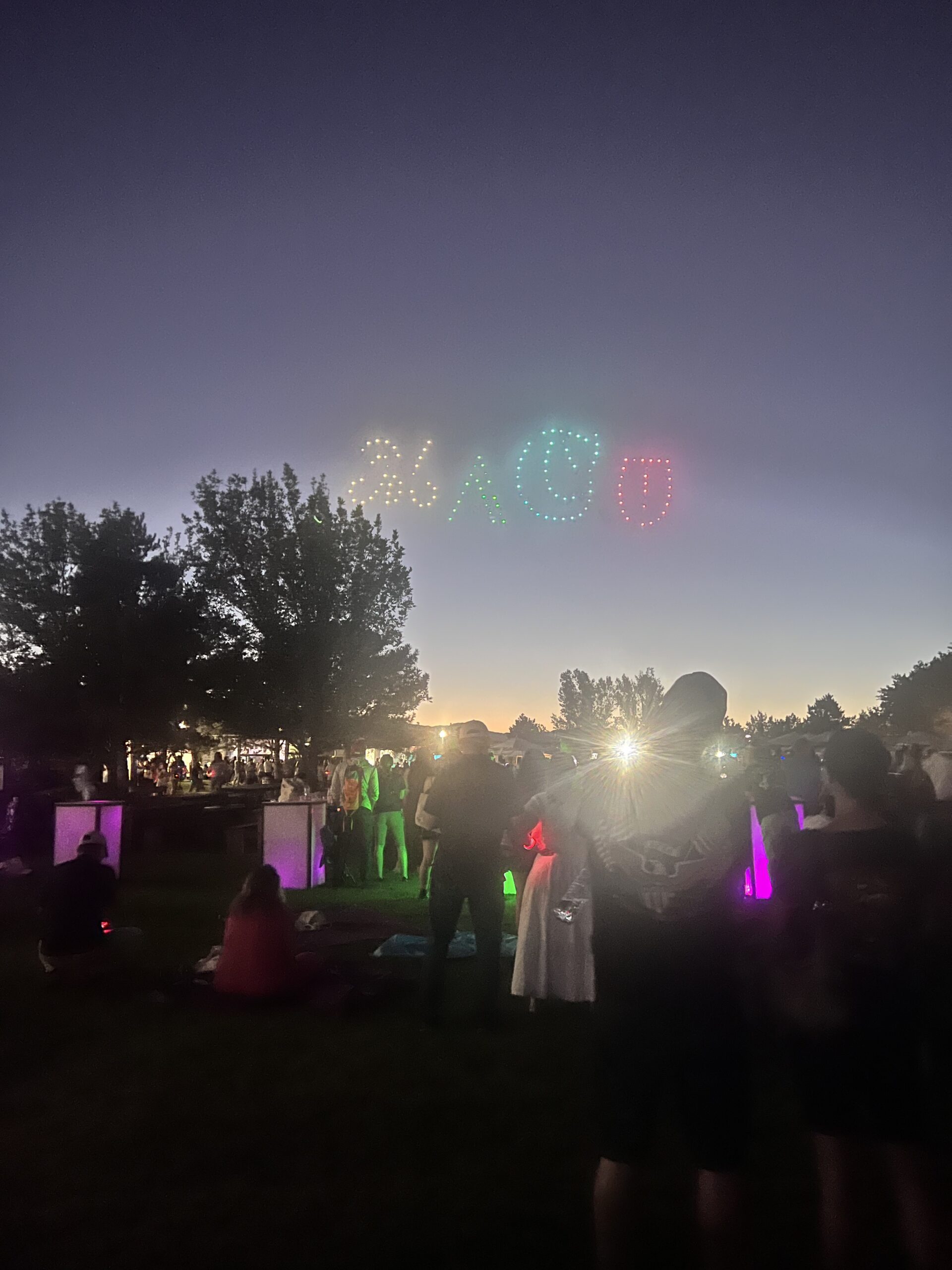 Drone light show spelling "MACU" in the night sky during MACU Fest 2025 at Thanksgiving Point, with a crowd watching from the lawn.