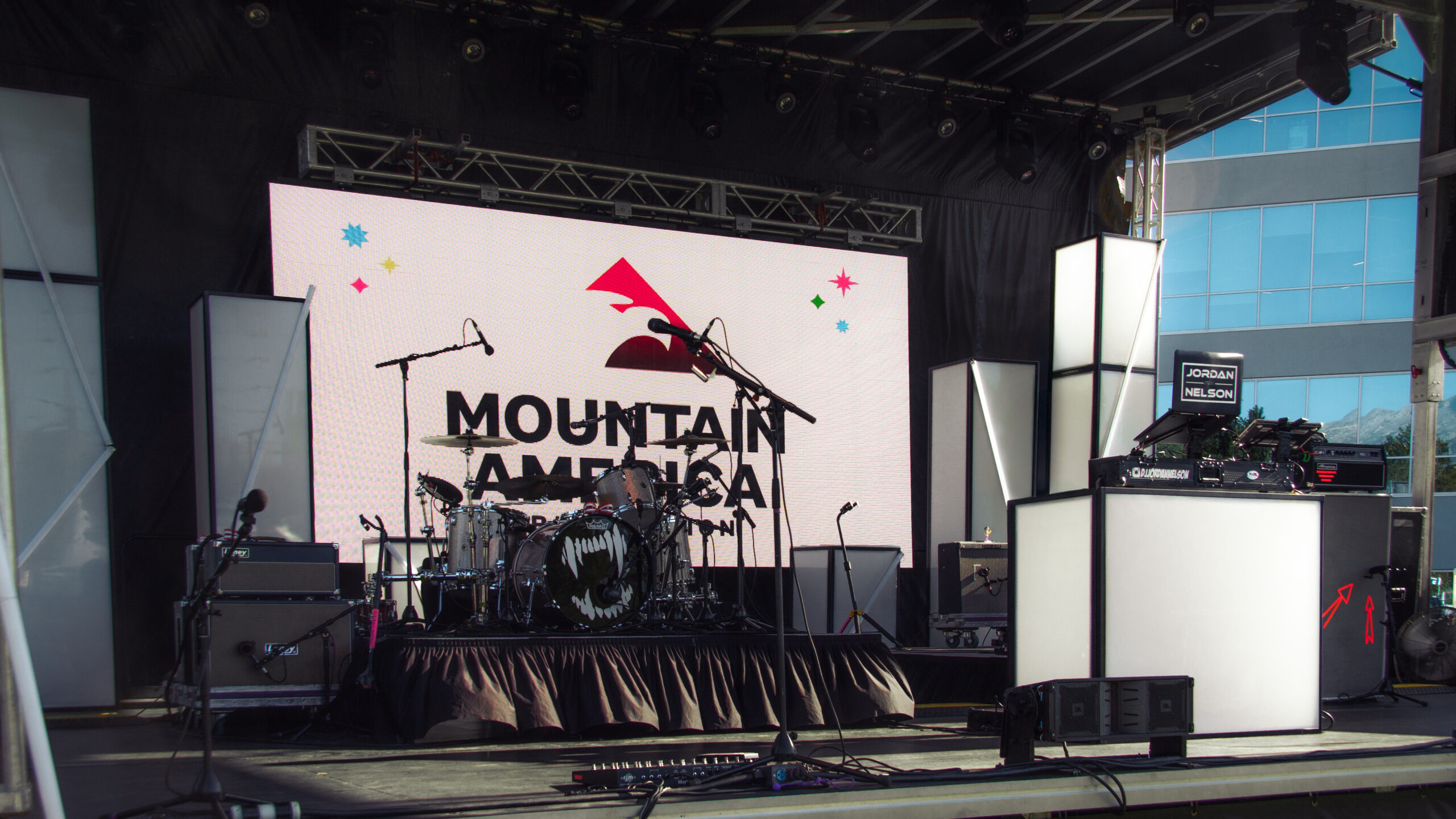 Corporate event stage setup by In The Event featuring an LED video wall, drum kit, DJ booth, and professional AV equipment for a live performance.