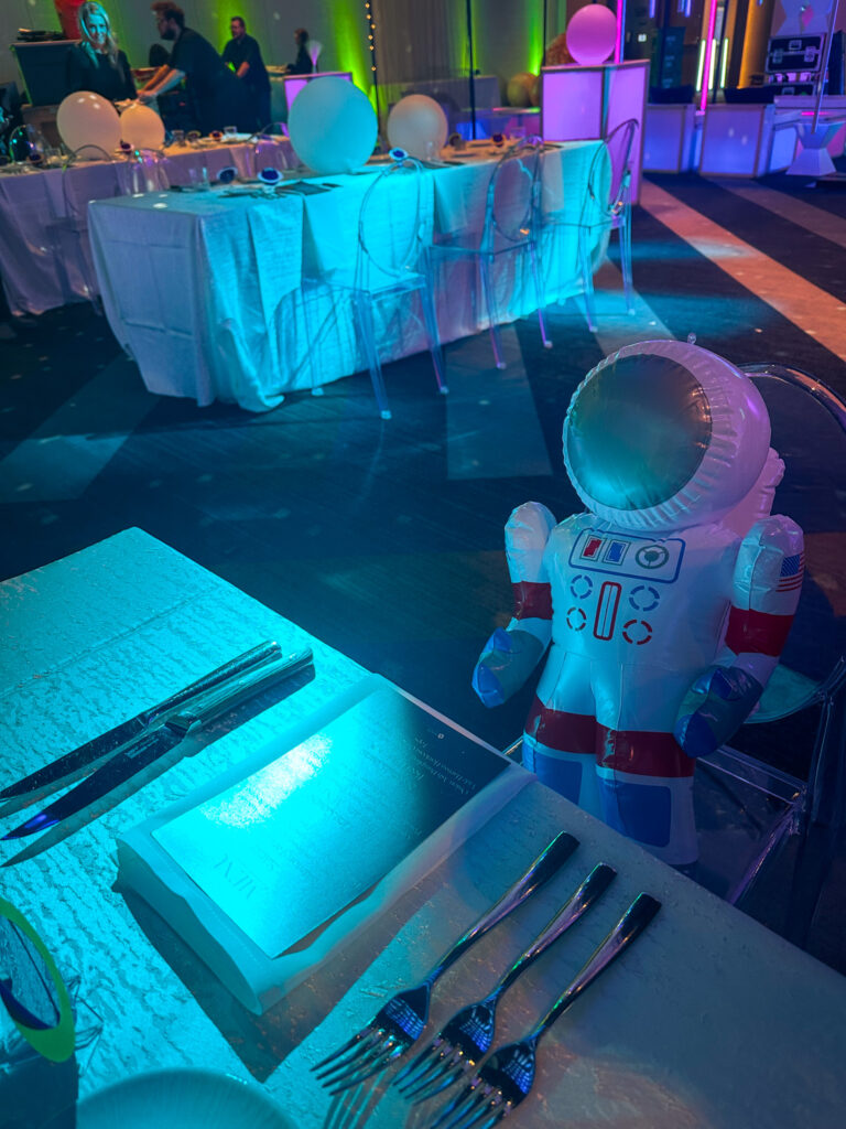 Space-themed dinner setup with glowing blue lighting, astronaut decor, and modern table settings at the Grand Hyatt Salt Lake City by In The Event.