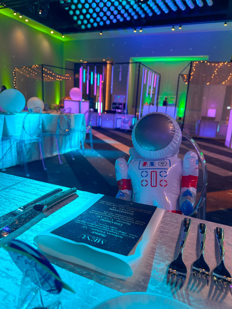 Space-themed dinner setup with glowing LED lighting, astronaut decor, and modern acrylic furniture at the Grand Hyatt Salt Lake City by In The Event.