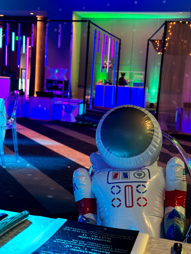 Inflatable astronaut decor seated at a table with glowing neon lighting and LED lounge structures in the background at the Grand Hyatt Salt Lake City event by In The Event.