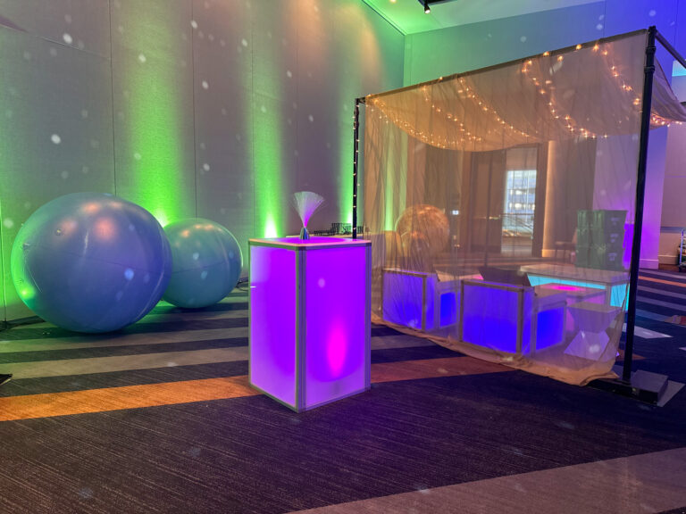 Space-themed lounge setup featuring glowing LED furniture, draped canopy with string lights, and oversized planetary spheres with ambient lighting at the Grand Hyatt Salt Lake City.