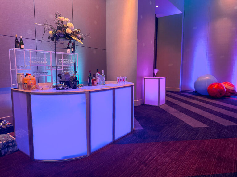 Illuminated curved LED bar setup with floral arrangement and colorful planetary props under purple and blue uplighting at Access DMC’s Grand Hyatt Salt Lake City event.