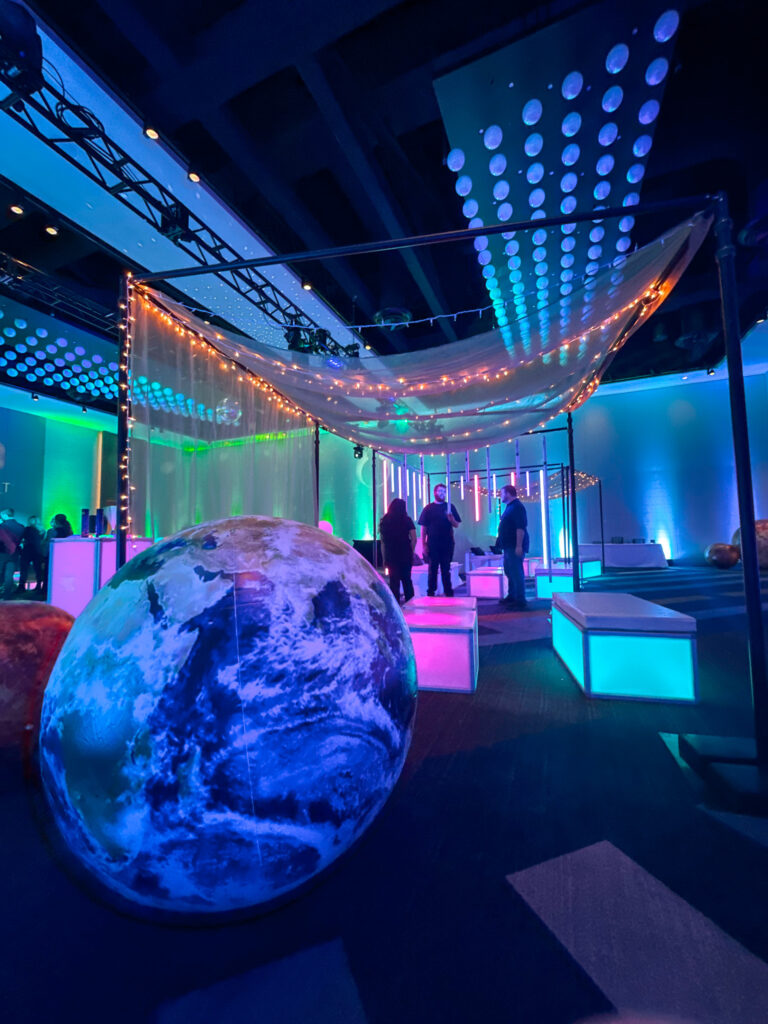 Illuminated lounge area featuring glowing modular furniture, planet props, and canopy draped with string lights during Access DMC’s space-themed event at the Grand Hyatt Salt Lake City.