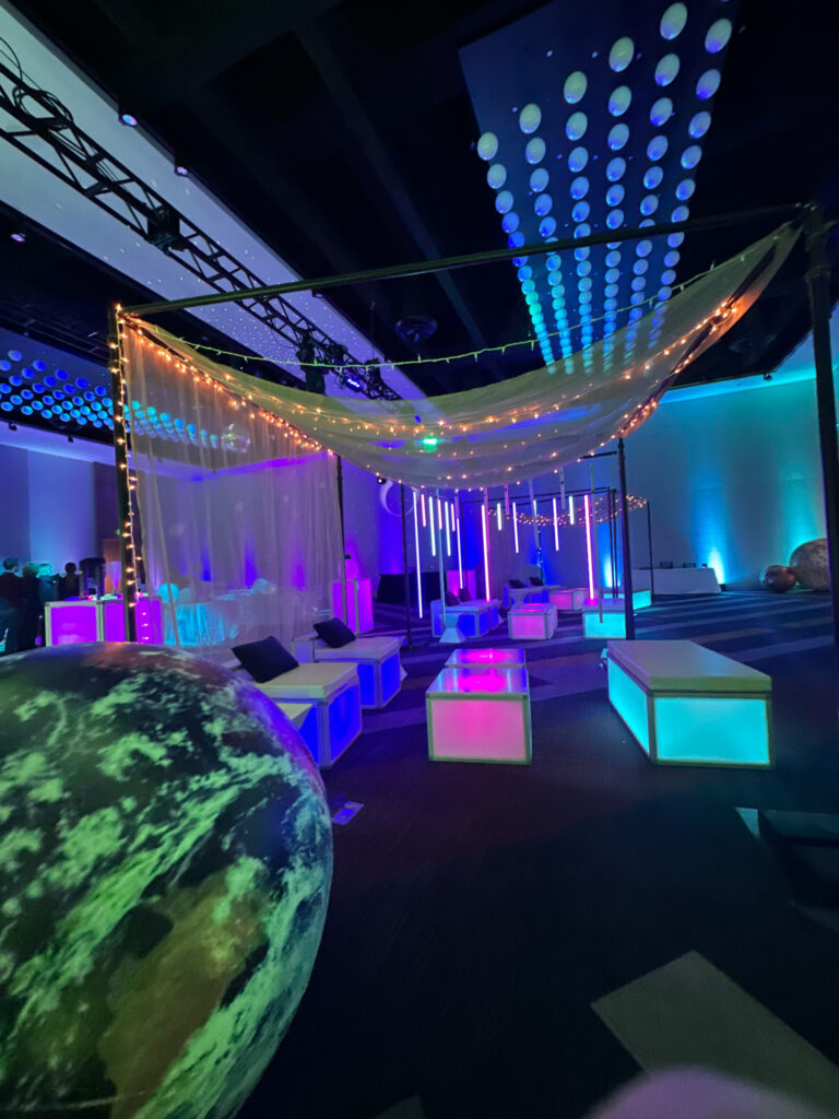 Illuminated lounge setup with glowing LED furniture, draped canopy lighting, and inflatable planet decor at Access DMC’s Grand Hyatt Salt Lake City event.
