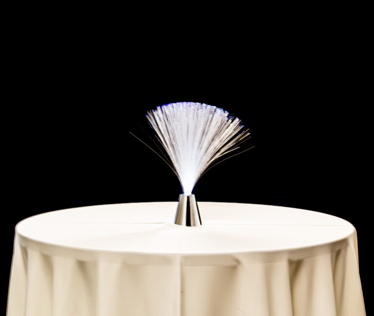 Illuminated fiber optic centerpiece glowing on a round cocktail table with white linen, perfect for modern LED event decor.