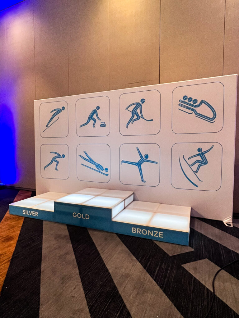 Illuminated gold, silver, and bronze podium setup with winter sports icons backdrop at the Access DMC x Thumbtack corporate event.