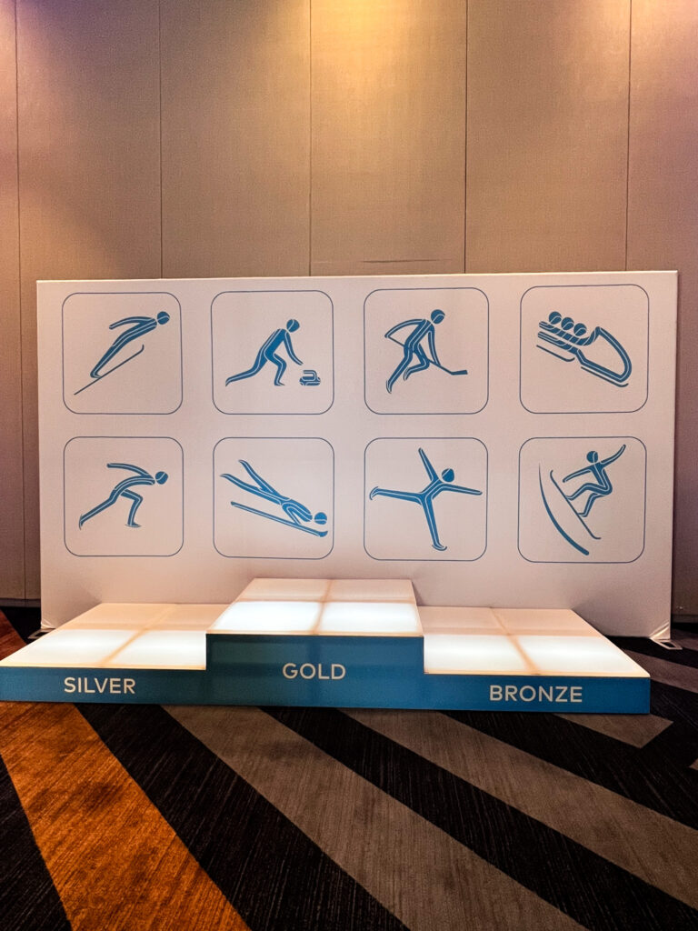 Illuminated podium with gold, silver, and bronze levels and a winter sports-themed backdrop at the Access DMC x Thumbtack corporate event.