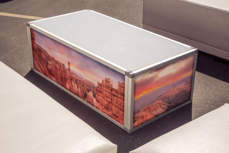 Close-up of a rectangular coffee table with custom, full-color, printed graphics featuring a scenic canyon landscape, part of a furniture rentals package.