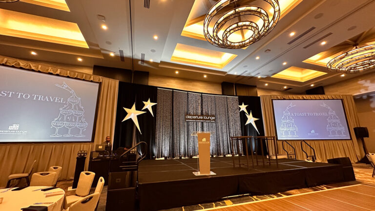 Wide view of a black stage rentals setup with layered event backdrops, large video projection screens for video rentals, custom event props (stars), and elegant overhead lighting rentals fixtures.