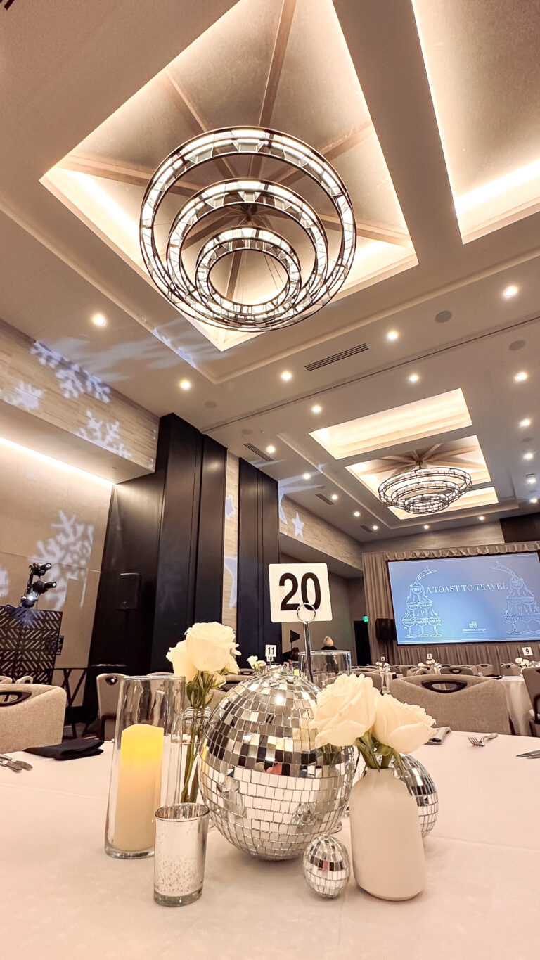 Close-up of elegant table setting featuring multiple disco ball centerpiece rentals, white roses, candles, a table number, and a modern chandelier lighting rentals fixture overhead.