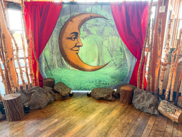 Vintage crescent moon backdrop framed by red velvet curtains with birch branches, faux rocks, and wood stumps at the High West Distillery Party