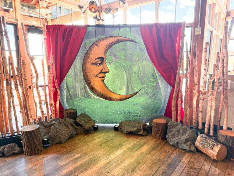 Crescent moon backdrop framed by red velvet curtains, birch tree trunks, and faux rocks on wood flooring at the High West Distillery Party