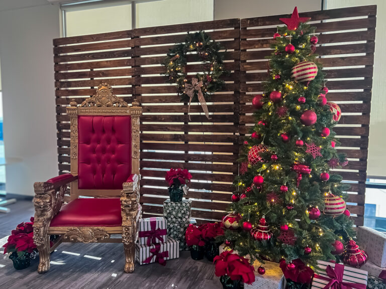 Gold Santa throne with red upholstery beside a decorated Christmas tree, wreath, and presents at the Trucordia holiday photo setup.