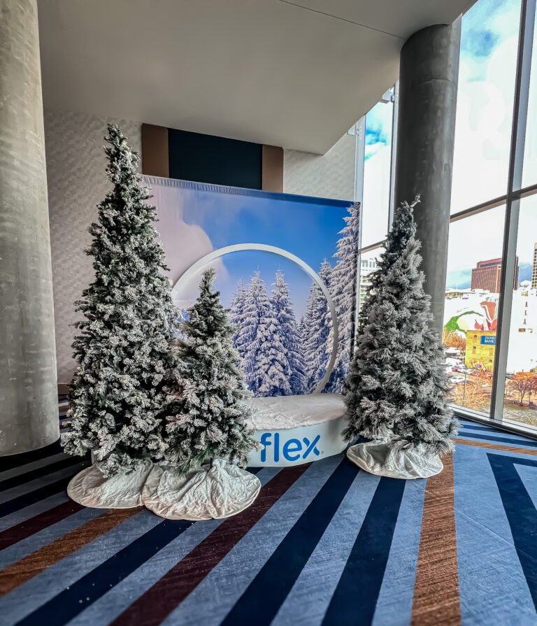 Snow globe photo booth with frosted pine trees and mountain backdrop near large windows at the Flex Holiday Party.