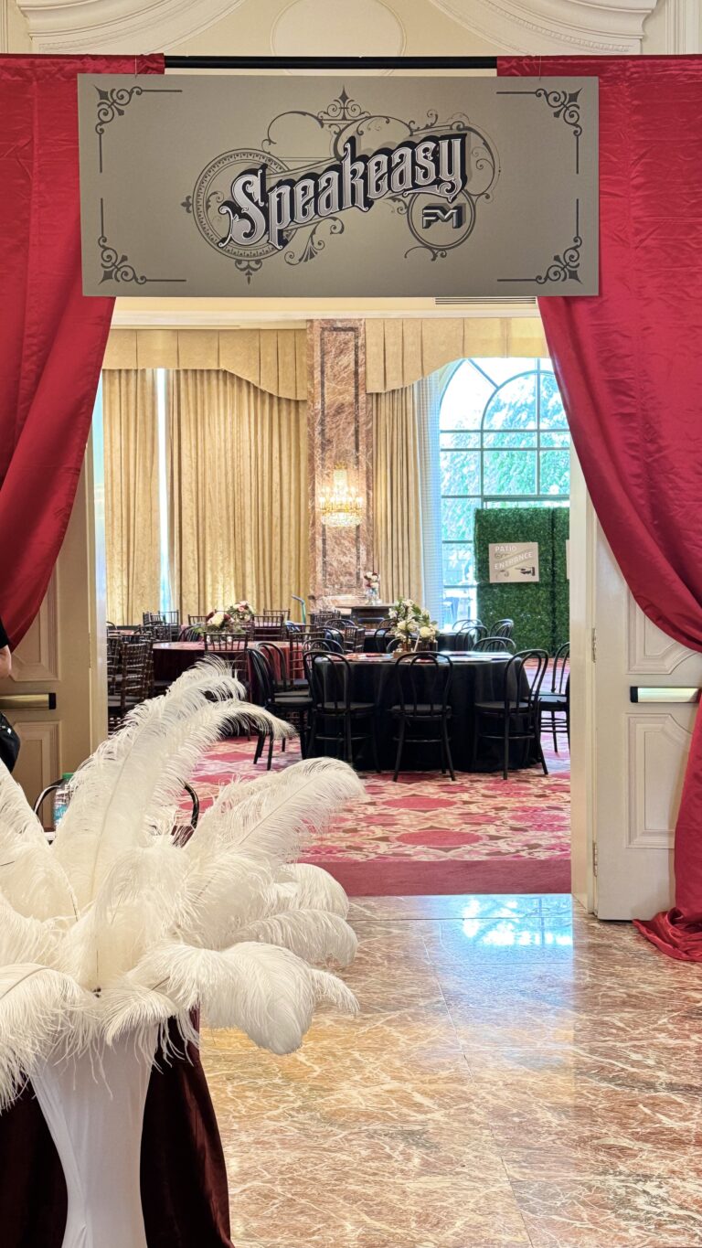 Elegant speakeasy event entrance featuring a vintage-style sign, red velvet curtains, and a white feather centerpiece leading into a lavish ballroom setup.