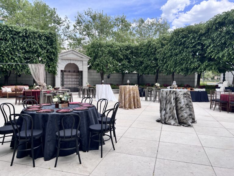 Elegant outdoor event with mixed seating, patterned linens, and floral centerpieces surrounded by lush greenery, styled by In The Event.