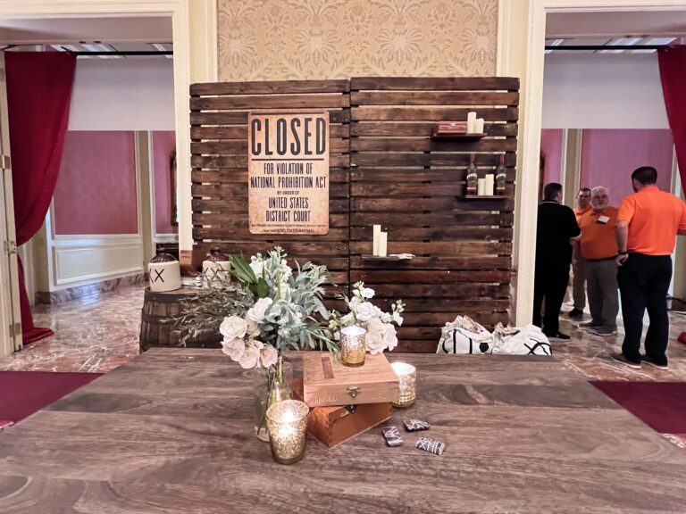 Rustic wood backdrop with “Closed for Violation of National Prohibition Act” sign, whiskey barrels, candles, and floral table arrangement designed by In The Event.