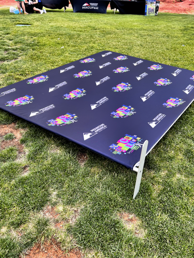 Step and repeat backdrop featuring Mountain America Credit Union MACU Fest logos lying on its side during event setup on grass