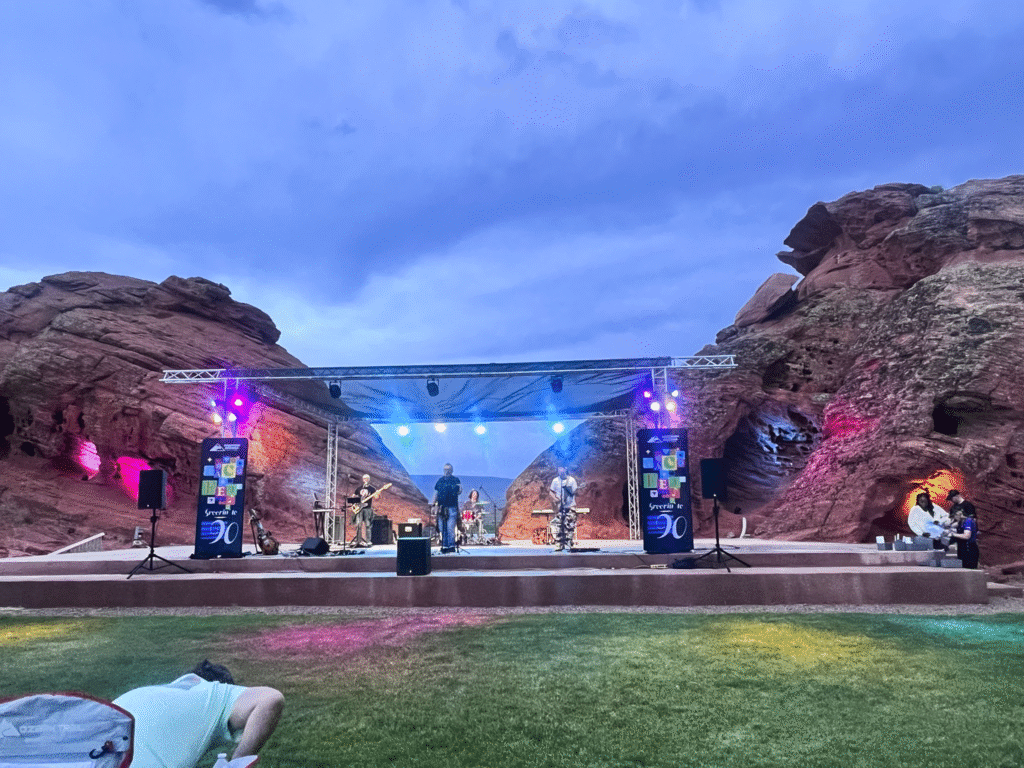 Evening concert at MACU Fest St. George featuring a live band on a truss-lit stage framed by red rock formations with colorful uplighting, produced by In The Event