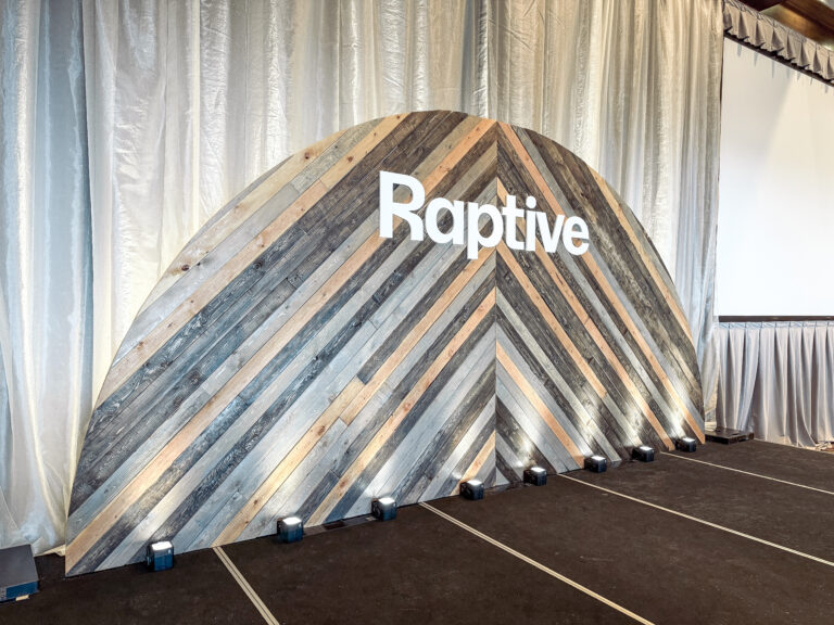 Corporate event stage featuring a semi-circle wood plank backdrop with custom signage.