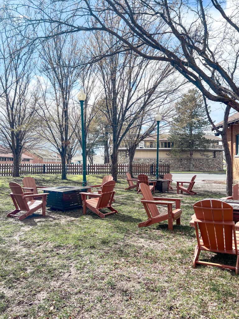 Wooden Adirondack chairs arranged around square fire pit tables with patio heaters outside a historic brick venue, designed by In The Event.