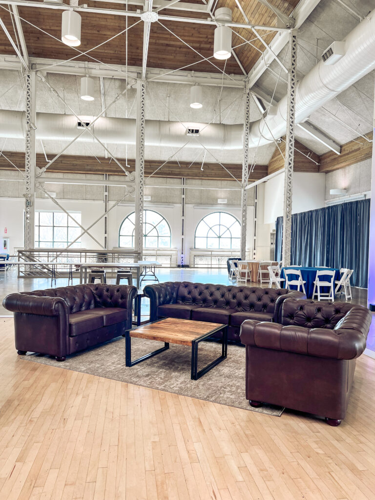 Elegant lounge area featuring dark brown tufted leather Chesterfield sofas and a wooden coffee table on a neutral rug by In The Event.