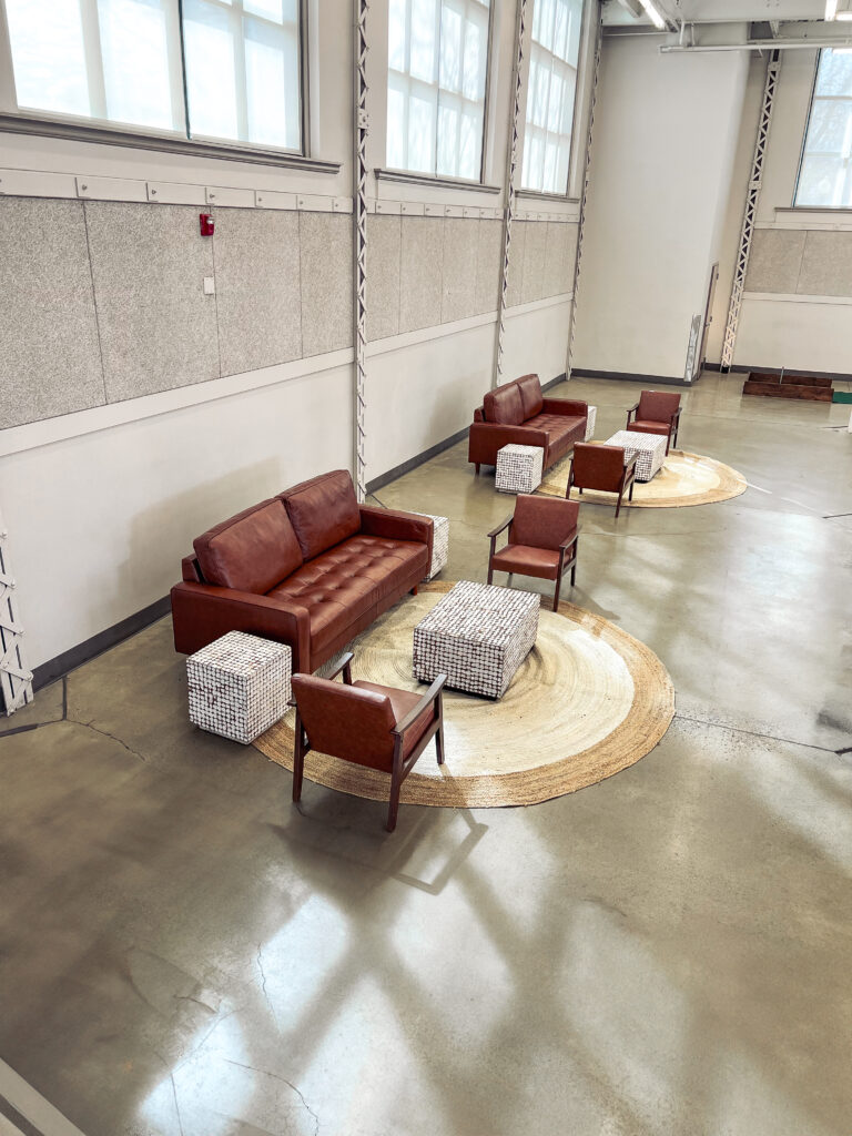 Modern lounge setup featuring brown leather sofa and armchairs with woven accent tables and a natural jute rug by In The Event.