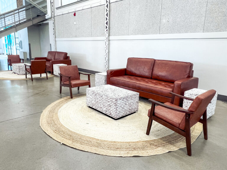 Modern lounge setup featuring brown leather sofa and armchairs with woven accent tables and a natural jute rug by In The Event.