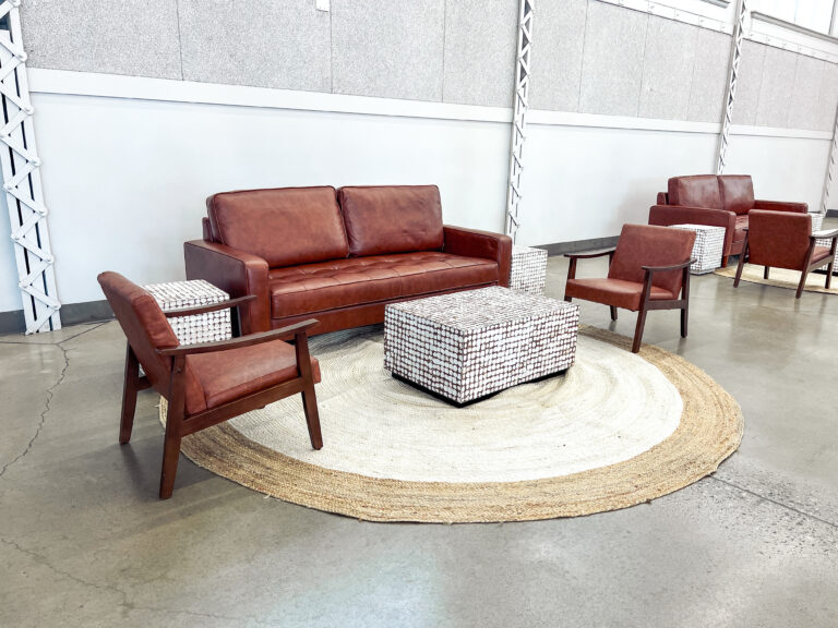 Modern lounge setup featuring brown leather sofa and armchairs with woven accent tables and a natural jute rug by In The Event.