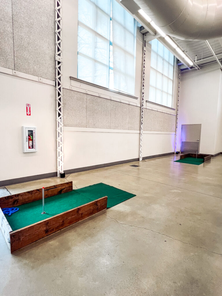Custom indoor mini golf course setup with green turf, wooden frames, and LED accent lighting for an interactive corporate event by In The Event.
