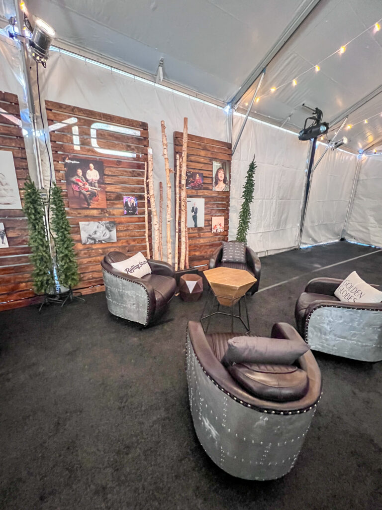 Modern industrial lounge design inside a tent featuring riveted aviator chairs, wood accent tables, and custom branded wood panel walls with birch pole décor.