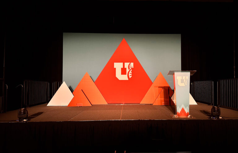 Custom stage design featuring branded geometric red and white event backdrops, with a matching acrylic podium for a corporate presentation.