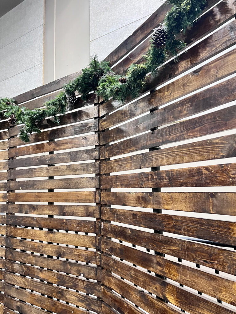 A professional event stage featuring a large rustic pallet wall with garland and pinecones serving as a seasonal event backdrop.