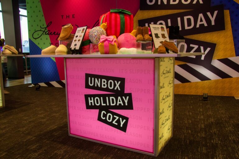 Festive holiday retail display featuring oversized ornament props, branded backdrop graphics, product merchandising, and custom event styling on a LED Deluxe Hiboy