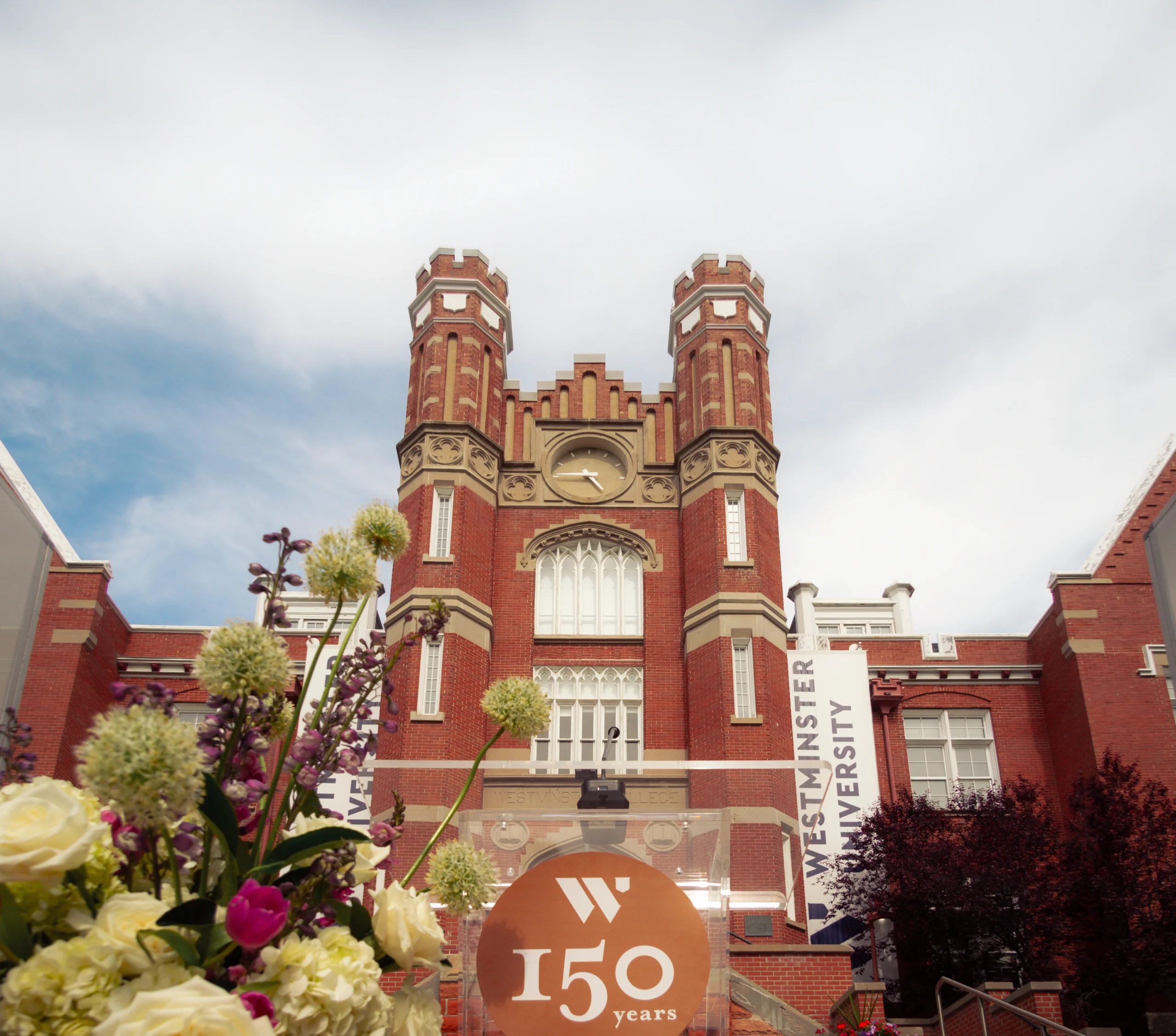 Westminster University — Converse Hall clock tower with 150th anniversary signage and foreground florals