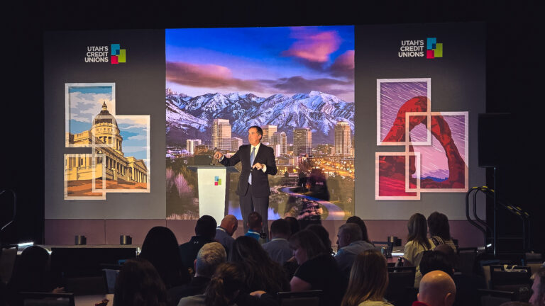 Conference speaker presenting on a custom-branded stage during the Utah Credit Union Association Credit Union Summit at Hyatt Regency Salt Lake City.