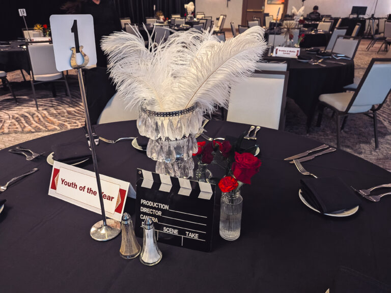 Hollywood-themed gala table centerpiece featuring white feathers, crystal accents, red roses, and movie-inspired décor at the Great Futures Gala.