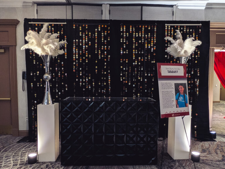 Hollywood-themed event bar featuring a black sequin backdrop, illuminated pedestals, feather centerpieces, and custom event signage at the Great Futures Gala.