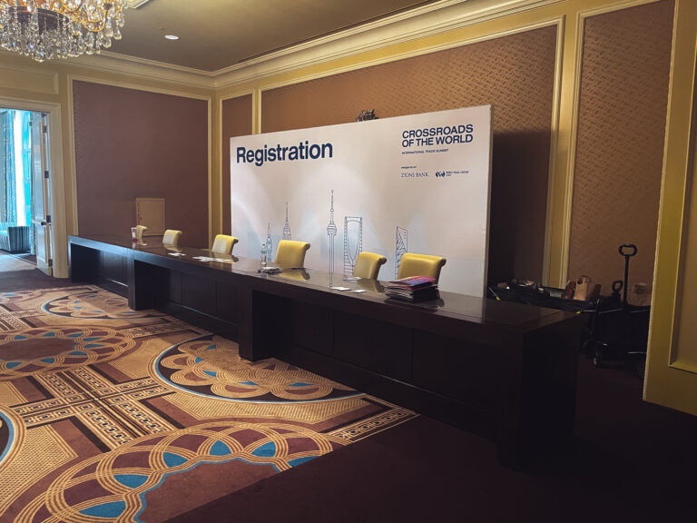 Custom registration desk and branded event check-in backdrop for the Crossroads of the World International Trade Summit at The Grand America Hotel.