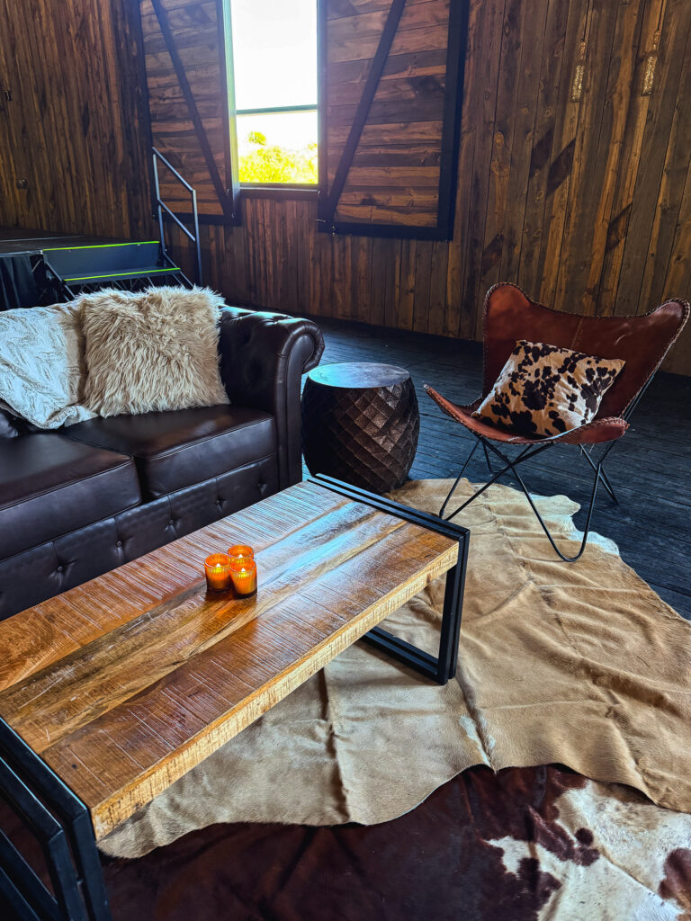 Western lounge seating at Lodges at Blue Sky featuring a brown leather sofa, leather butterfly chair, rustic wood coffee table, and cowhide rug.
