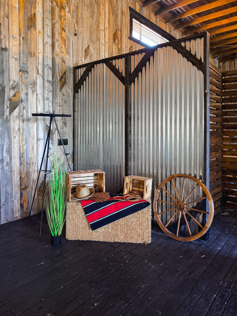 Western photo backdrop featuring corrugated metal panels, hay bales, a wagon wheel, wooden crates, and rustic props at Lodges at Blue Sky.