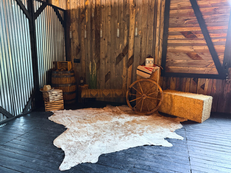 Western-themed decor vignette featuring hay bales, a wagon wheel, whiskey barrel, cowhide rug, and rustic accents at Lodges at Blue Sky.