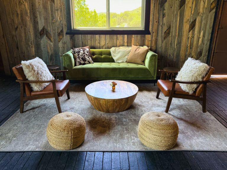 Western-inspired lounge featuring a green velvet sofa, leather chairs, wood coffee table, and rustic décor.