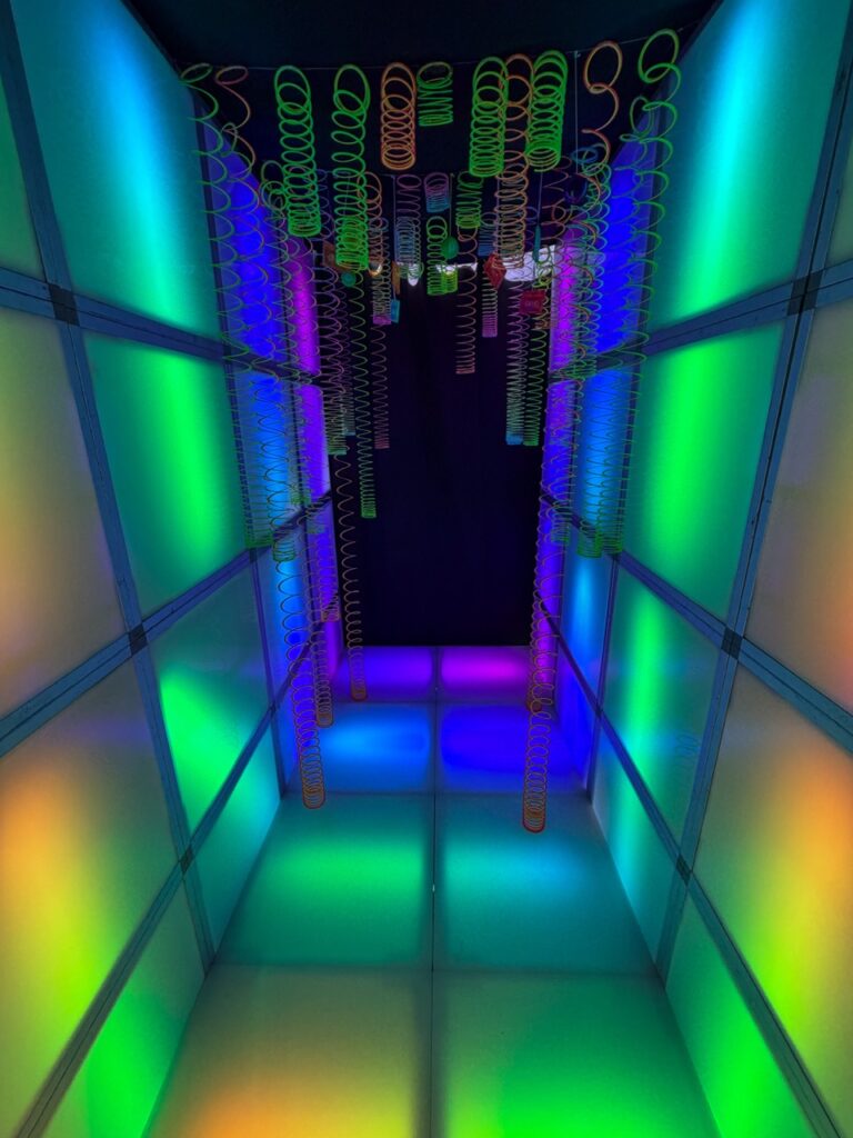 Illuminated LED tunnel featuring glowing wall panels, color-changing floor tiles, and hanging neon springs for an immersive event entrance.