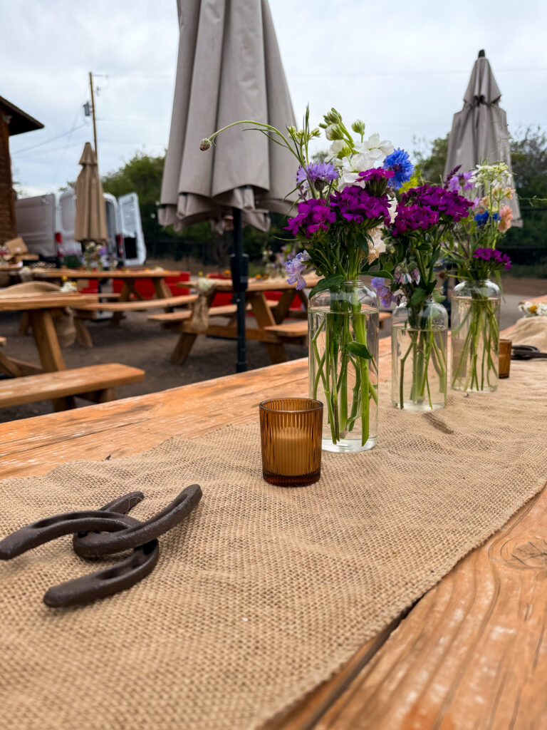 Rustic outdoor farm table styled with burlap runners, wildflower centerpieces, horseshoes, and amber votive candles at The Lodge at Blue Sky.