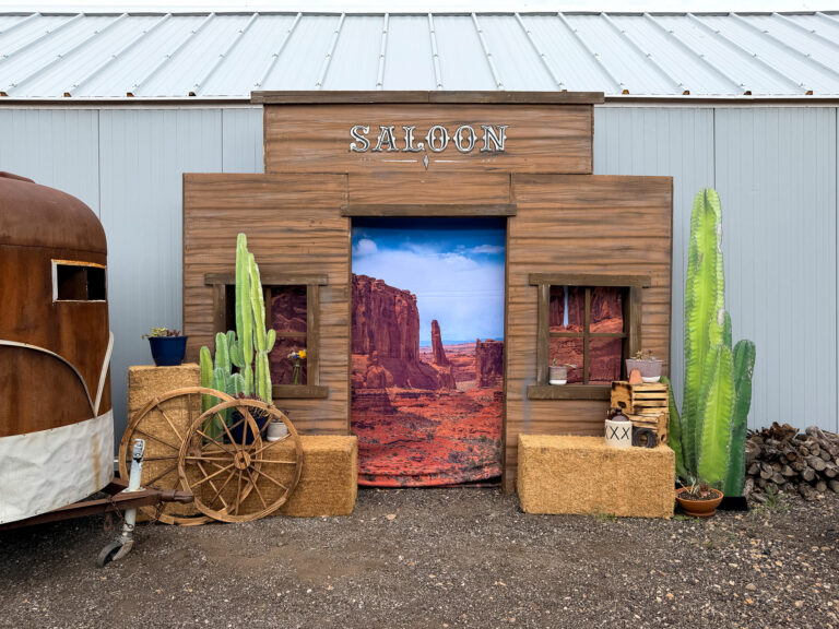 Custom Western saloon photo backdrop with hay bales, wagon wheels, cacti, and rustic decor at The Lodge at Blue Sky.