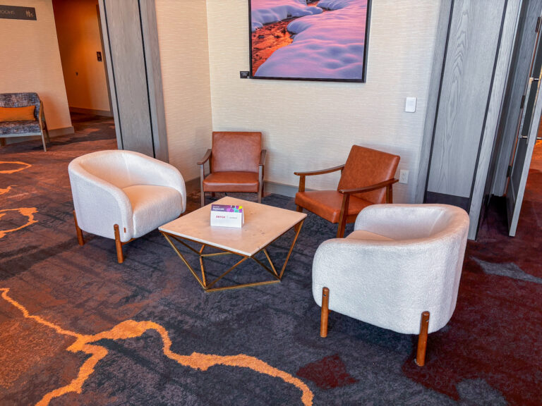 Contemporary event lounge featuring white Clara lounge chairs, tan leather accent Dylan chairs, and a square marble coffee table with a gold geometric base by In The Event.