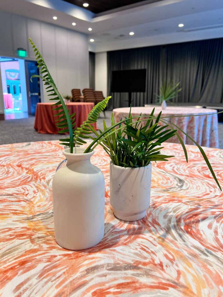 Minimalist tropical centerpiece with white ceramic vases on a custom patterned table linen at a corporate event designed by In The Event.