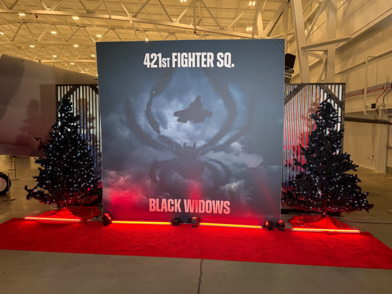 Custom "421st Fighter Squadron Black Widows" branded photo backdrop with red carpet, illuminated Christmas trees, and dramatic uplighting at the Hill Aerospace Museum.